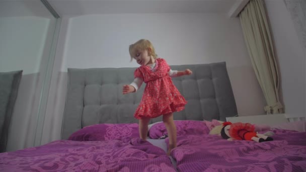 Boldog szőke lány vörös ruhában jumping az ágyon