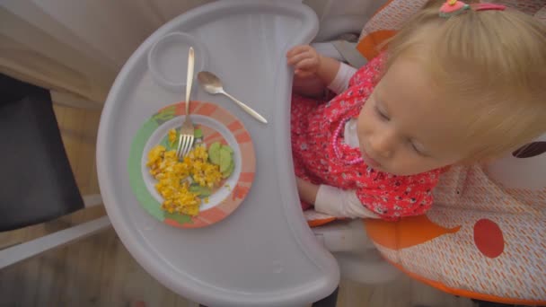 Мила дівчинка їсть яйця в дитячому кріслі — стокове відео