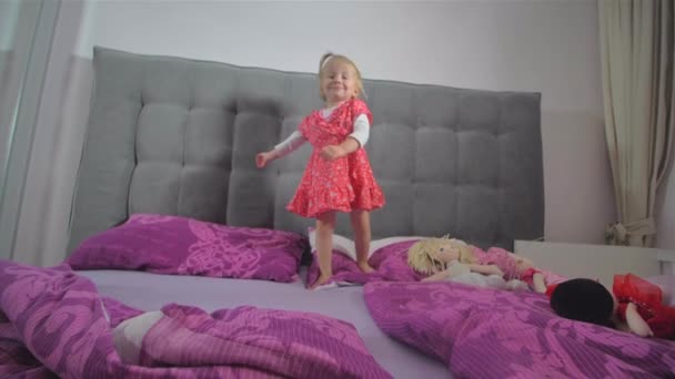 Счастливая блондинка в красном платье прыгает на кровати — стоковое видео