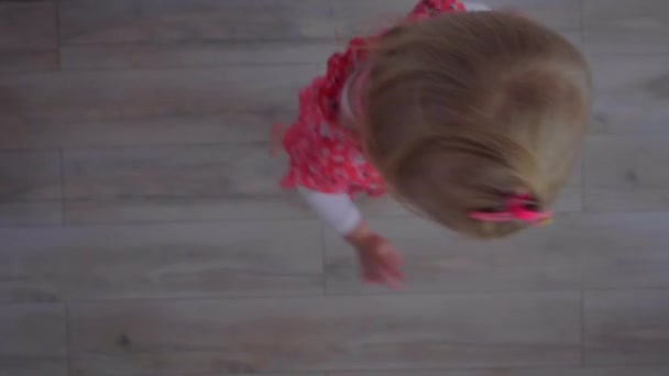 Kırmızı elbise ile küçük bir sarışın kız dönüyor ve dans — Stok video