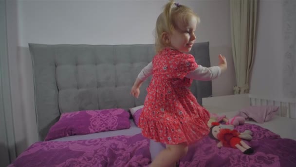 Šťastná blondýnka s červenými šaty poskakující po posteli — Stock video