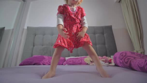 Menina loira feliz com vestido vermelho pulando na cama — Vídeo de Stock