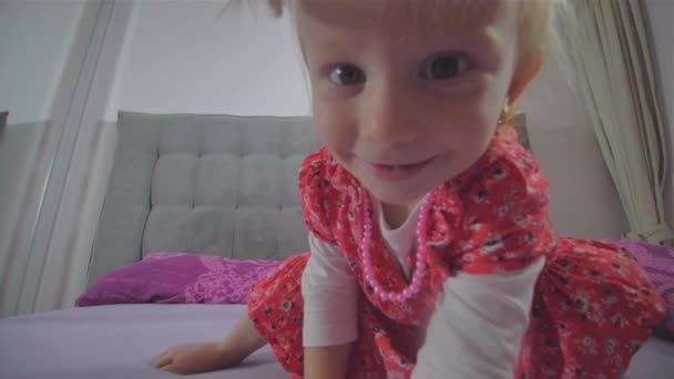 Gelukkig blond meisje met rode jurk springen op het bed — Stockvideo