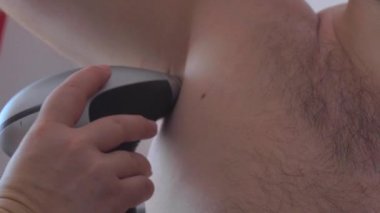  Bir adam evde epilasyon için lazer epilatör kullanır. Koltuk altı Fotoepilasyon.