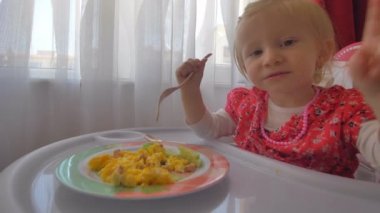Bir bebek sandalyesinde omlet yiyen sevimli küçük bir kız