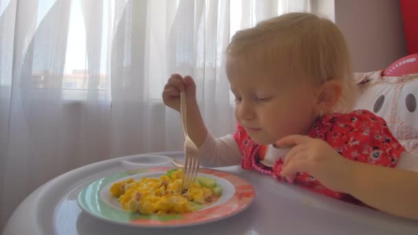 Een schattig klein meisje eten roerei in een baby stoel — Stockvideo