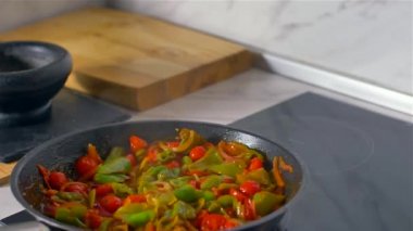 Mutfakta çalışan şef, karışık renkli sebzeler tavada kavrulur.