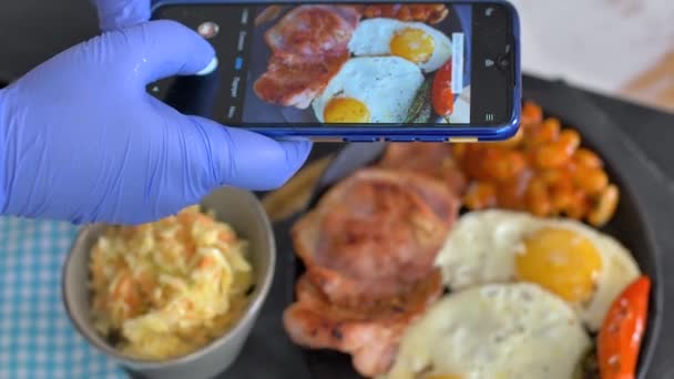 Женщина в ресторане фотографирует еду с помощью камеры мобильного телефона. Сэндвич с яичницей и авокадо — стоковое видео