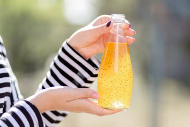 Çizgili ceketli bir kız elinde meyve suyu olan cam bir şişe tutuyor. Kızın çok güzel bir manikürü ve siyah beyaz bir ceketi var. Çekirdekli portakal suyu. Bottel 'e odaklan