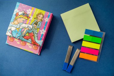 stationery on a blue background,  colored stickers, lead, a notebook. top view