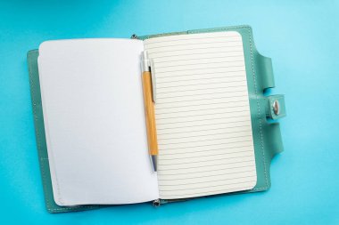 Arka planda bir cetvelde açık bir defter. Kalem not defterinde.