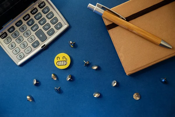 stationery on a blue background, an eraser, a gray calculator, a wood pen, pushpins. top view