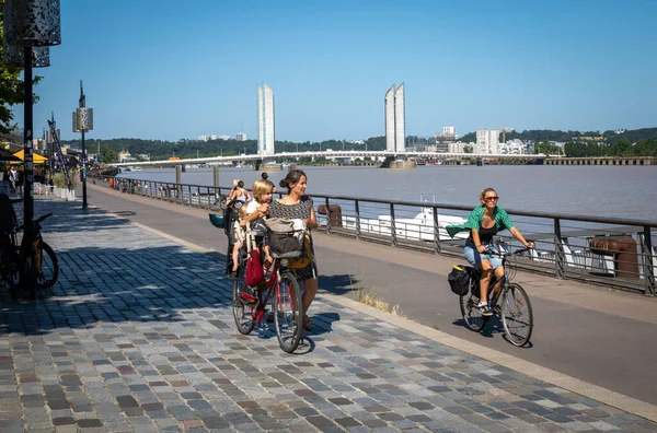 Çocuklarıyla birlikte Garonne nehrinin yanında bisiklet süren bir kadın ve Fransa 'nın Bordeaux kentinde Jacques Chaban Delmas köprüsü..