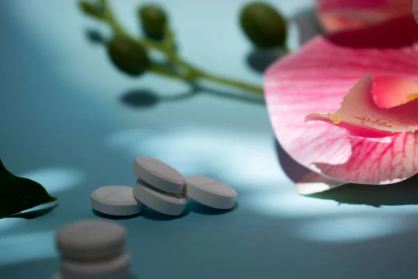 Mavi bir zemin üzerinde spa ve sağlıklı dekoratif unsurlar, hafif ışıklandırma ve sağlık, ilaç, rahatlama veya sağlık yaşam tarzı kavramları için ideal minimalist bir kompozisyon içeren birkaç beyaz hapın ya da diyet takviyelerinin makro fotoğrafı..