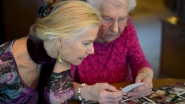 Yaşlı bir kadın kızıyla birlikte fotoğraflara bakıyor. Kıdemli kadın yemek odasında oturmuş kızıyla fotoğraflarına bakıyor. Beyin eğitimi. Bellek etkinliği.