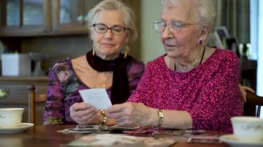 Yavaş çekim, düşük açı, son derece yakın çekim. Yaşlı mutlu kadın, eski fotoğraflara bakıyor ve kızıyla yemek masasında geçirdiği anıları hatırlıyor..