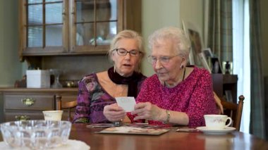 Mutlu yaşlı yaşlı kadın kızıyla fotoğraflara bakıyor. Kıdemli kadın yemek odasında oturmuş kızıyla fotoğraflarına bakıyor. Beyin eğitimi. Bellek etkinliği.