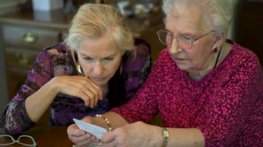 Yaşlı bir kadın kızıyla birlikte fotoğraflara bakıyor. Kıdemli kadın yemek odasında oturmuş kızıyla fotoğraflarına bakıyor. Beyin eğitimi. Bellek etkinliği.