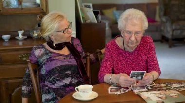 Mutlu yaşlı yaşlı kadın kızıyla fotoğraflara bakıyor. Kıdemli kadın yemek odasında oturmuş kızıyla fotoğraflarına bakıyor. Beyin eğitimi. Bellek etkinliği.