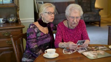 Mutlu yaşlı kadın kızıyla fotoğraflara bakıyor. Kıdemli kadın yemek odasında oturmuş kızıyla fotoğraflarına bakıyor. Beyin eğitimi. Bellek etkinliği.