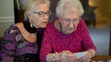 Yaşlı bir kadın kızıyla birlikte fotoğraflara bakıyor. Kıdemli kadın yemek odasında oturmuş kızıyla fotoğraflarına bakıyor. Beyin eğitimi. Bellek etkinliği.