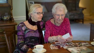 Mutlu yaşlı kadın kızıyla fotoğraflara bakıyor. Kıdemli kadın yemek odasında oturmuş kızıyla fotoğraflarına bakıyor. Beyin eğitimi. Bellek etkinliği.