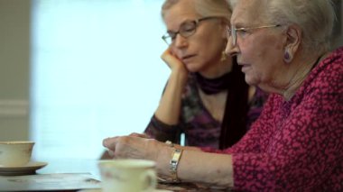 Yaşlı bir kadın kızıyla birlikte fotoğraflara bakıyor. Kıdemli kadın yemek odasında oturmuş kızıyla fotoğraflarına bakıyor. Beyin eğitimi. Bellek etkinliği.