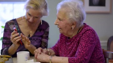 Orta yaşlı kızıyla aynı masada oturan mutlu yaşlı bir kadın. Ailesini ya da seyahat fotoğraflarını telefonla izliyor. Gülümseyen sarışın kadın. Yaşlı dinleyen, akıllı telefon kullanan..