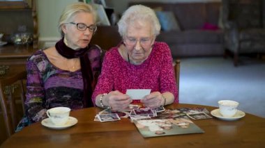 Mutlu yaşlı kadın kızıyla fotoğraflara bakıyor. Kıdemli kadın yemek odasında oturmuş kızıyla fotoğraflarına bakıyor. Beyin eğitimi. Bellek etkinliği.