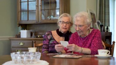 Mutlu yaşlı yaşlı kadın kızıyla fotoğraflara bakıyor. Kıdemli kadın yemek odasında oturmuş kızıyla fotoğraflarına bakıyor. Beyin eğitimi. Bellek etkinliği.