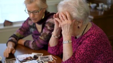 Yaşlı bir kadın kızıyla birlikte fotoğraflara bakıyor. Kıdemli kadın yemek odasında oturmuş kızıyla fotoğraflarına bakıyor. Beyin eğitimi. Bellek etkinliği.