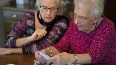 Yaşlı bir kadın kızıyla birlikte fotoğraflara bakıyor. Kıdemli kadın yemek odasında oturmuş kızıyla fotoğraflarına bakıyor. Beyin eğitimi. Bellek etkinliği.