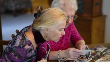 Yaşlı bir kadın kızıyla birlikte fotoğraflara bakıyor. Kıdemli kadın yemek odasında oturmuş kızıyla fotoğraflarına bakıyor. Beyin eğitimi. Bellek etkinliği.