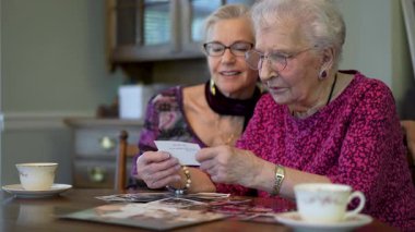 Yavaş çekim, düşük açı, son derece yakın çekim. Yaşlı mutlu kadın, eski fotoğraflara bakıyor ve kızıyla yemek masasında geçirdiği anıları hatırlıyor..