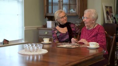 Mutlu yaşlı yaşlı kadın yemek odasında kızıyla fotoğraflara bakıyor. Aileyle fotoğraflara bakıyorum. Beyin eğitimi. Bellek etkinliği.