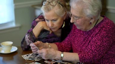 Yaşlı ve mutlu bir kadının eski fotoğraflara bakıp kızıyla yemek masasında geçirdiği anıları hatırlaması..