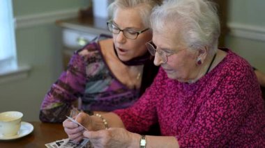 Yaşlı ve mutlu bir kadının eski fotoğraflara bakıp kızıyla yemek masasında geçirdiği anıları hatırlaması..