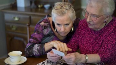 Yaşlı ve mutlu bir kadının eski fotoğraflara bakıp kızıyla yemek masasında geçirdiği anıları hatırlaması..