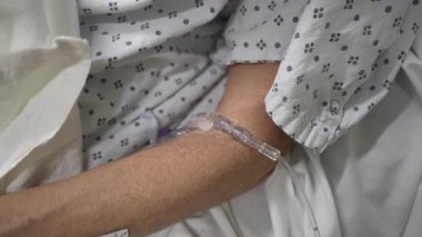 Olgun bir kadın hastane yatağında dinleniyor, acil serviste serum tedavisi görüyor, yoğun bakım ortamını ve durumunu vurguluyor..