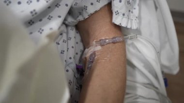 Olgun bir kadın hastane yatağında, kolunda serumla tıbbi bakım görüyor. Etrafı acil servis personeliyle çevrili..