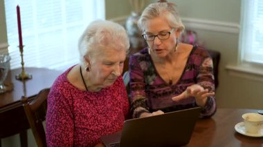 Yaşlı bir kadının yanında yetişkin bir kızı olan bilgisayara bakması, birlikte vakit geçirmekten ve öğrenmekten zevk alması..