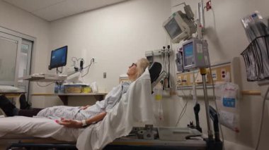 Winchester, VA, ABD - 09 03 2025: Olgun bir kadın hastane yatağında tedavi görürken rahat bir şekilde dinleniyor. Oda izleme için çeşitli tıbbi cihazlarla donatılmıştır..