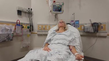 Winchester, VA, ABD - 09 03 2025: Olgun bir kadın hastane yatağında yatıyor, yakınlardaki çeşitli izleme ekipmanlarıyla tıbbi yardım alıyor, konfor ve bakımına odaklanıyor.