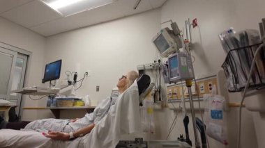 Winchester, VA, ABD - 09 03 2025: Olgun bir kadın hastane yatağında tedavi görüyor ve tıbbi ekipmanlar etrafını sarmış durumda. Oda aydınlık, sağlanan bakımı vurguluyor..