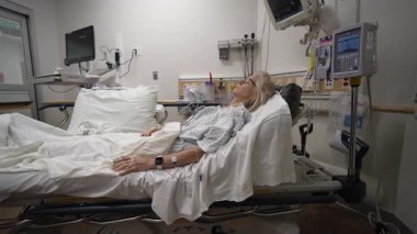 Winchester, VA, ABD - 09 03 2025: Olgun bir kadın acil serviste bir hastane yatağında yatıyor, klinik bir ortamda tıbbi personelden bakım ve izleme görüyor.