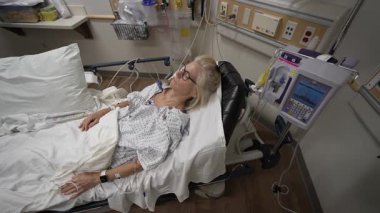 Winchester, VA, ABD - 09 03 2025: Olgun bir kadın bir hastane yatağında, sağlık önlüğü giyerken, bir acil serviste monitörler ve tıbbi ekipmanlarla çevrili olarak dinleniyor.