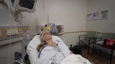 Winchester, VA, ABD - 09 03 2025: Olgun bir kadın acil serviste bir hastane yatağında yatıyor, klinik bir ortamda tıbbi personelden tedavi ve bakım görüyor.