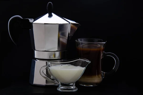 cup of coffee, milk jug and a coffee pot. Black background.