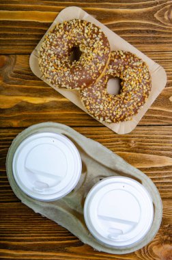 Kahve için kağıt bardak, tek kullanımlık ekolojik kahve malzemeleri. Kağıt tepsilerde çörekler. Tahta masa. Üstte görüntü.