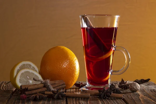 Svařované víno s pomerančovou kůrou, skořicovými tyčinkami a anýzem a citrusy na dřevěném stole na oranžovém pozadí. — Stock fotografie